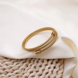Eleganter mehrschichtiger Goldspiral-Armreif auf weißer Seide und geflochtener Matte