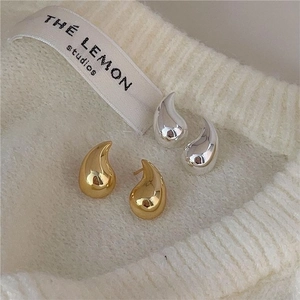 Close-up of minimalist gold and silver teardrop earrings on white knit background
