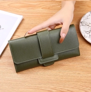 Close-up of a long dark green leather wallet held by hand on a wooden desk background
