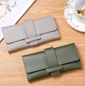 Detail of grey and green litchi grain leather wallets with buckle on wooden table