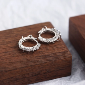 Macro shot of silver-toned hoop earrings with inlaid zircons on a dark wood block