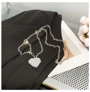 Detail view of silver heart pendant with chunky chain on black fabric background