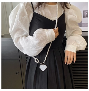 Detail of the pearl chain and white heart pendant on a black and white pleated dress