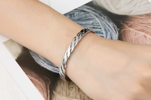 Close-up of a silver twisted stainless steel bangle on wrist with a polished mirror finish