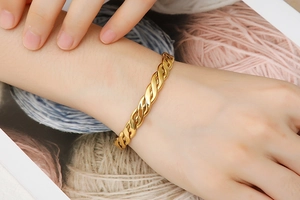 Close-up of golden twisted mesh bangle on wrist with warm background tones