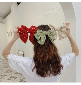 Close-up of three oversized polka dot bow clips in red, green, and beige fabric material