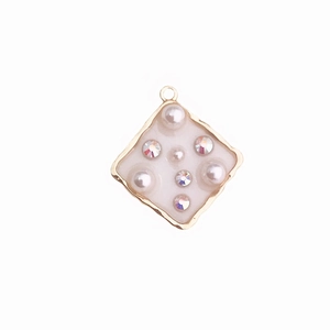 Detail of gold rhombus pendant with white enamel, pearls and sparkling rhinestones