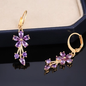 Detail showing purple zircon flower drop earrings with elegant gold plating on black mirror