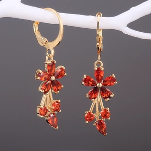 Macro view of gold flower tassel earrings with red zirconia on a white branch