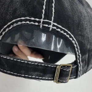 Détail d'une casquette en denim noir avec coutures blanches et boucle en laiton