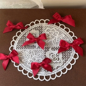 Set of six red satin bow hair clips displayed on a white lace coaster with brown background