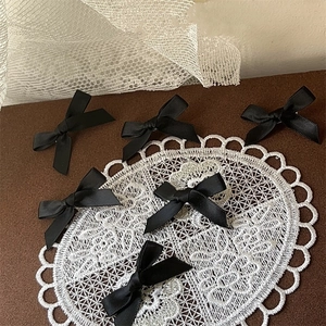 Detail view of six handmade black satin ribbon bow hair clips on elegant lace background