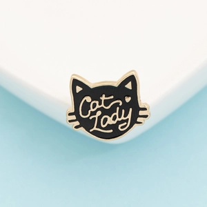Detail of a black enamel cat head brooch with gold Cat Lady lettering and metal edges