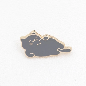 Macro shot of a sleeping grey cat enamel pin with golden metallic outlines on a textured base