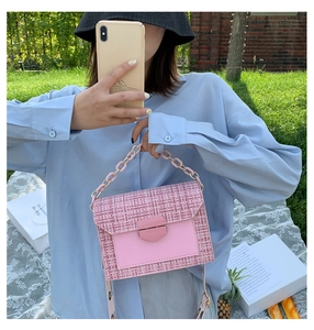 Detail of pink tweed chain bag with metal buckle held by hand in a casual outdoor setting