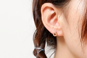 Close-up of rose gold screw head stud earring worn by a model on a white background