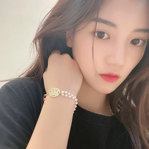 Detailed shot of double-row pearl bracelet with a golden vintage coin charm on wrist