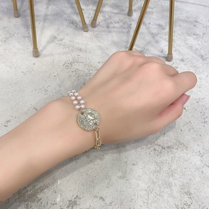 Detail of a layered pearl bracelet with a vintage metal coin pendant and chunky chain links