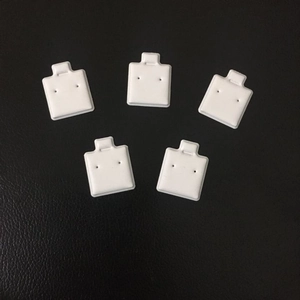 Five pieces of white square PVC earring display cards on black textured leather surface
