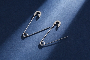 Dramatic lighting showcasing silver safety pin earrings with a polished metallic finish