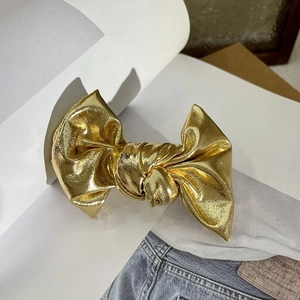 Detailed view of a shiny gold metal bow hair clip with textured metallic finish