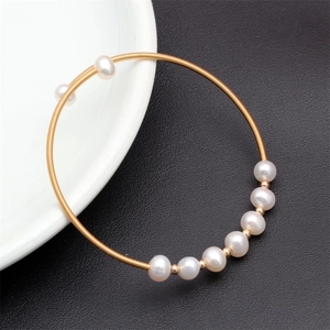 Close-up of golden elastic bangle featuring nine white pearls and gold metal coils