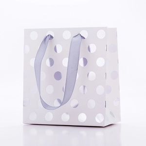 White paper gift bag with silver foil polka dots and metallic ribbon handles on white base