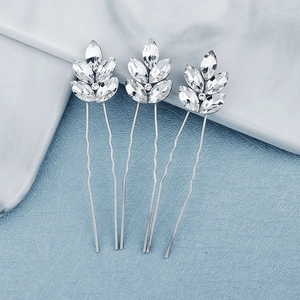 Detail of three silver bridal hair pins with leaf-shaped rhinestones on a blue texture