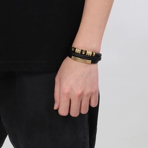 Detail of multilayer black braided leather bracelet with golden metal accents on wrist