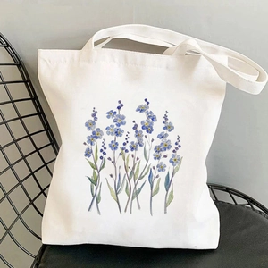 White canvas tote bag with blue floral watercolor painting on a stylish metal chair