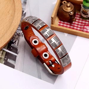 Detail of a brown leather punk bracelet with geometric metal accents on a wooden tray