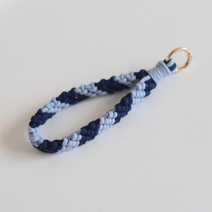 Detail of hand-woven striped wrist strap in blue with a gold metal key ring