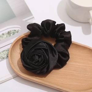 Detailed view of a black satin rose hair scrunchie on a wooden tray with a lifestyle background