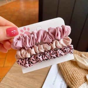 Three assorted fabric hair scrunchies in pink, beige, and leopard print on display card