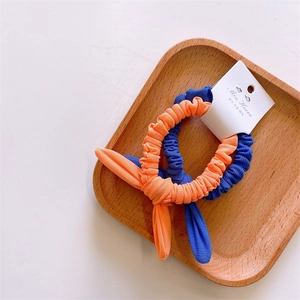 Close-up of ribbed knit bunny ear hair ties in blue and orange on a wooden tray