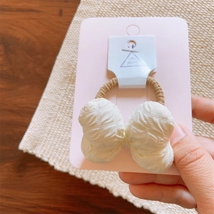Detail view of cream quilted fabric bow hair tie with elastic band on display card