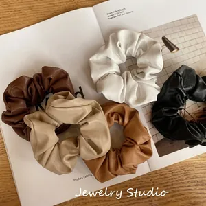 Detailed view of 5 faux leather scrunchies in earth tones displayed on an open magazine