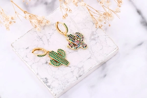 Detailed view of cactus-shaped gold earrings with colorful zircon stones on marble