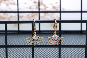 Detail of gold fan-shaped drop earrings with colorful zircon stones on a black wire rack