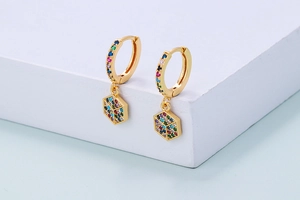 Detail of colorful zircon inlaid gold earring with hexagonal pendant on white stand