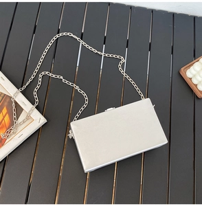Detail of silver metallic box clutch with thin chain strap on dark wooden surface