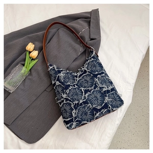 Blue denim tote bag with white floral embroidery and brown leather strap on white linen