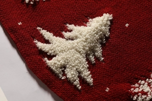 Close-up of red knitted Christmas tree skirt with white plush tree pattern detail