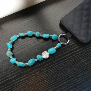 Crossbody phone strap with turquoise beads and silver pendant on dark wood