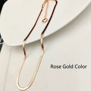 Detail of rose gold snake bone chain with a delicate heart pendant on white ceramic