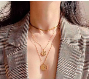 Detailed view of triple-layered gold snake chain and coin necklaces on checkered blazer
