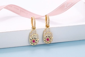 Detail of gold Hamsa earrings with colorful zircon stones and pink heart center stone