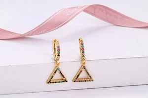 Macro detail of gold triangle earrings with colorful zircon stones on a white stand