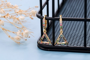 Detail of gold-plated triangle earrings with colorful zircon stones on a black basket