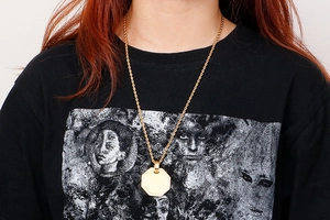 Close-up of a gold octagonal pendant with a twist chain worn over a black sweatshirt